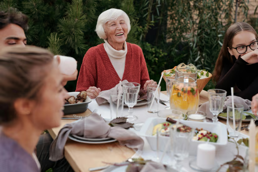 Happy family gathering around dinner table with elderly woman laughing